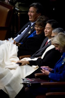 UNITED STATES - JANUARY 20: Reps. Mark Takano, D-Calif., left, Alma Adams, D-N.C., and other members, huddle under a blanket in the Capitol's House chamber before President Barack Obama's State of the Union address, January 20, 2015. (Photo By Tom Williams/CQ Roll Call)