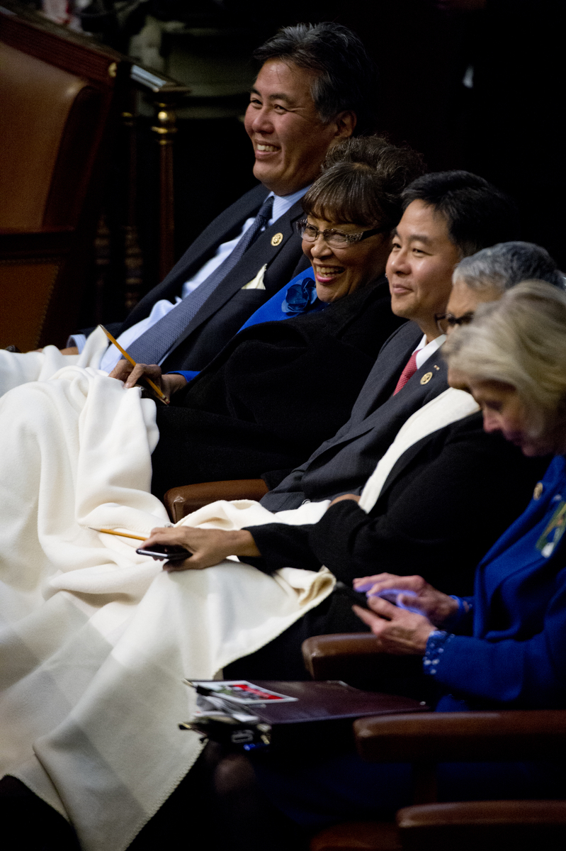 UNITED STATES - JANUARY 20: Reps. Mark Takano, D-Calif., left, Alma Adams, D-N.C., and other members, huddle under a blanket in the Capitol's House chamber before President Barack Obama's State of the Union address, January 20, 2015. (Photo By Tom Williams/CQ Roll Call)